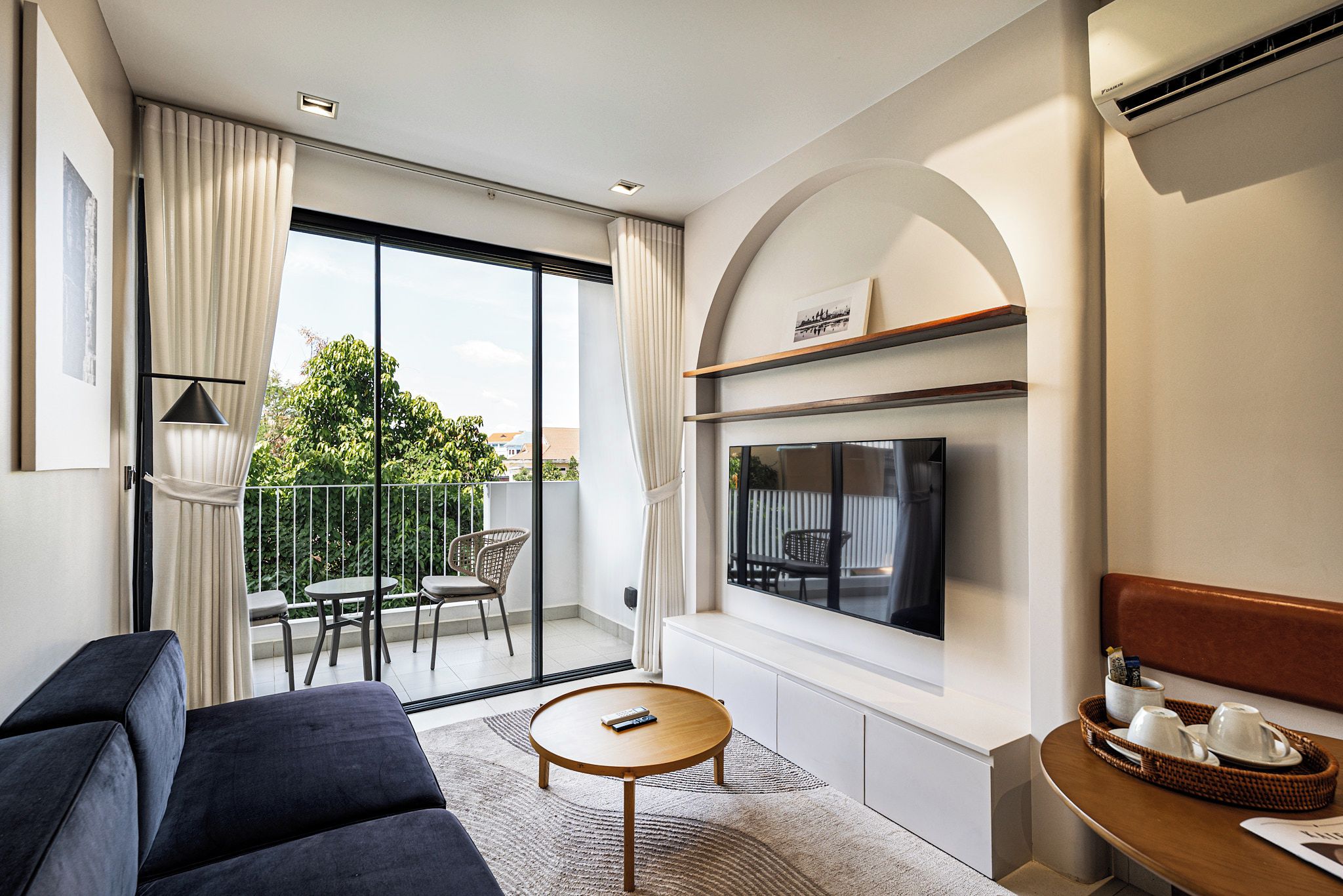 Une chambre d’hôtel moderne dotée d’une grande télévision, d’un canapé, d’une petite table ronde et d’un balcon offrant une vue sur la verdure.