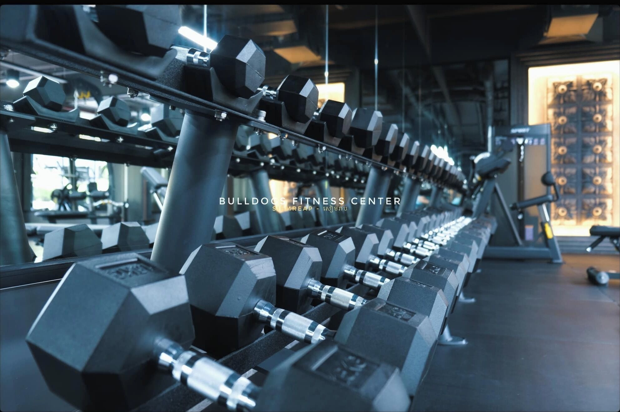 A gym with multiple rows of dumbbells and exercise equipment.