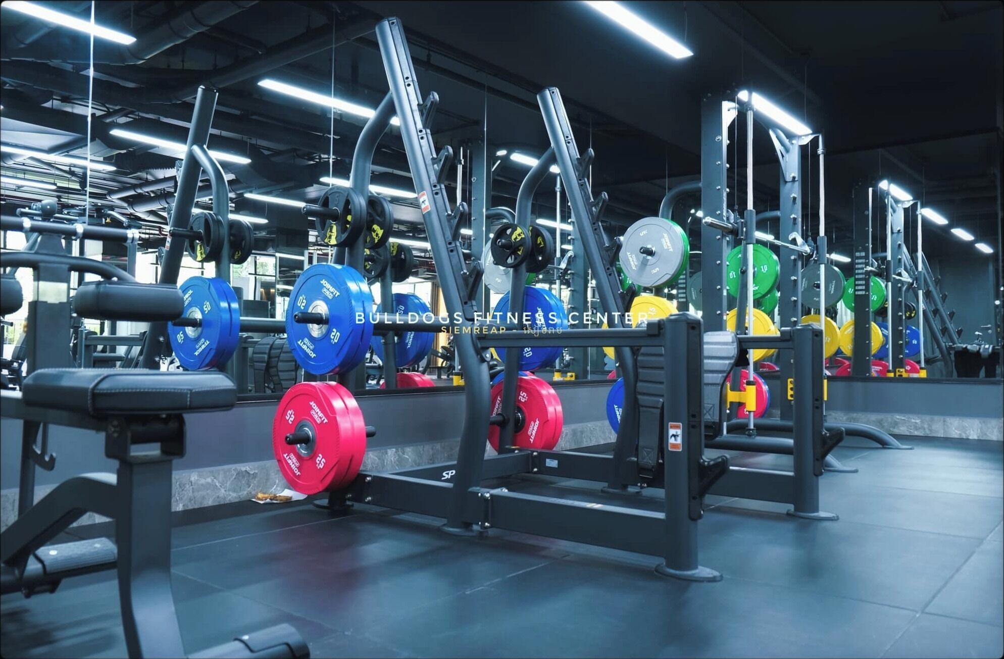 A gym with weightlifting equipment and a mirrored wall.