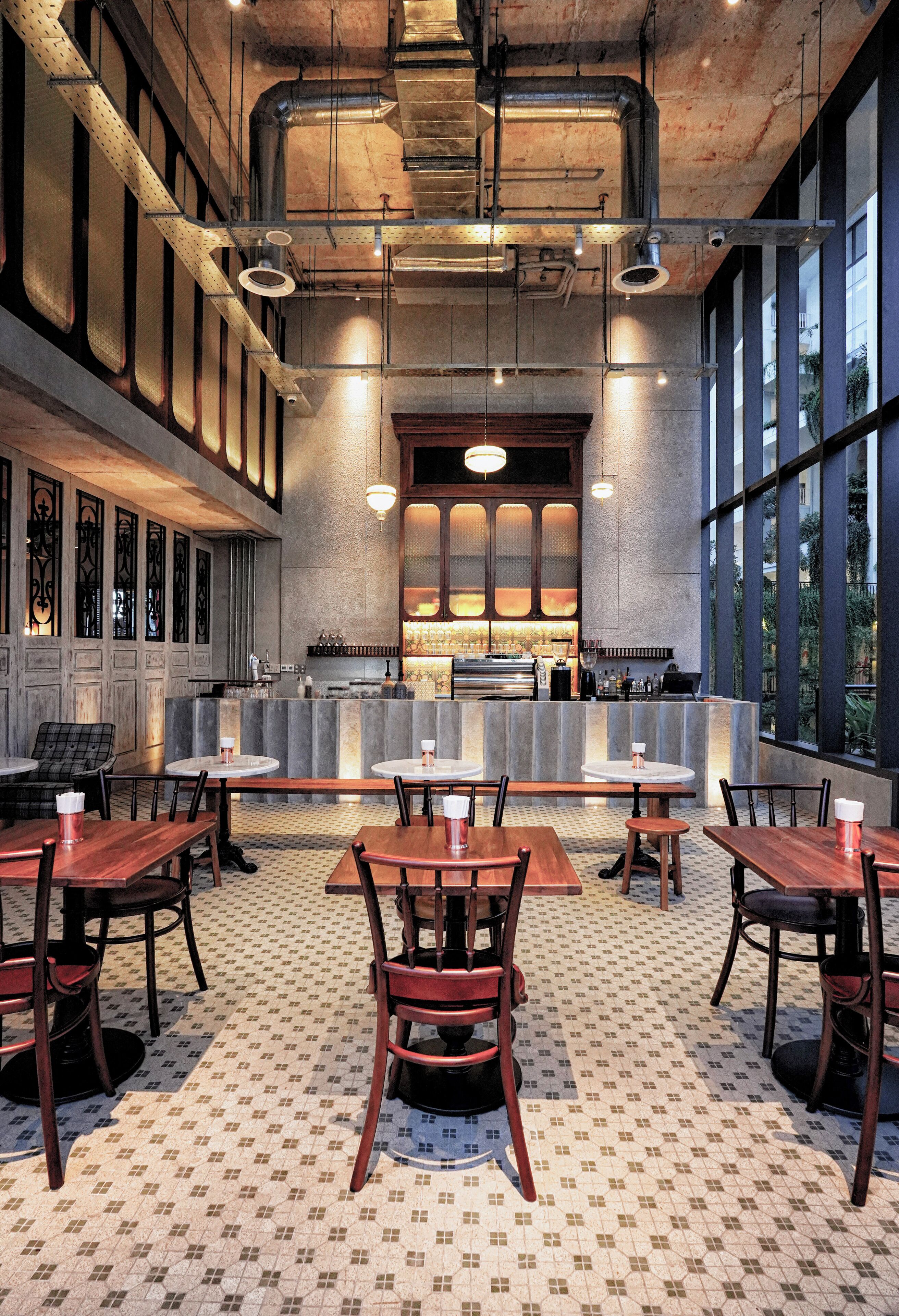 A restaurant with high ceilings, exposed ductwork, and large windows. Tables and chairs are arranged for dining.