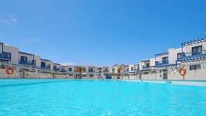 Una piscina con agua cristalina azul, rodeada de edificios blancos con detalles azules y balcones.