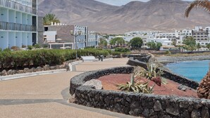 Un complejo turístico frente al mar con piscina, muros de piedra y vistas a montañas.