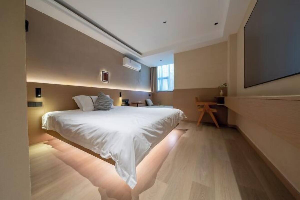 A modern bedroom with a bed, bedside tables, a desk, and a large window.