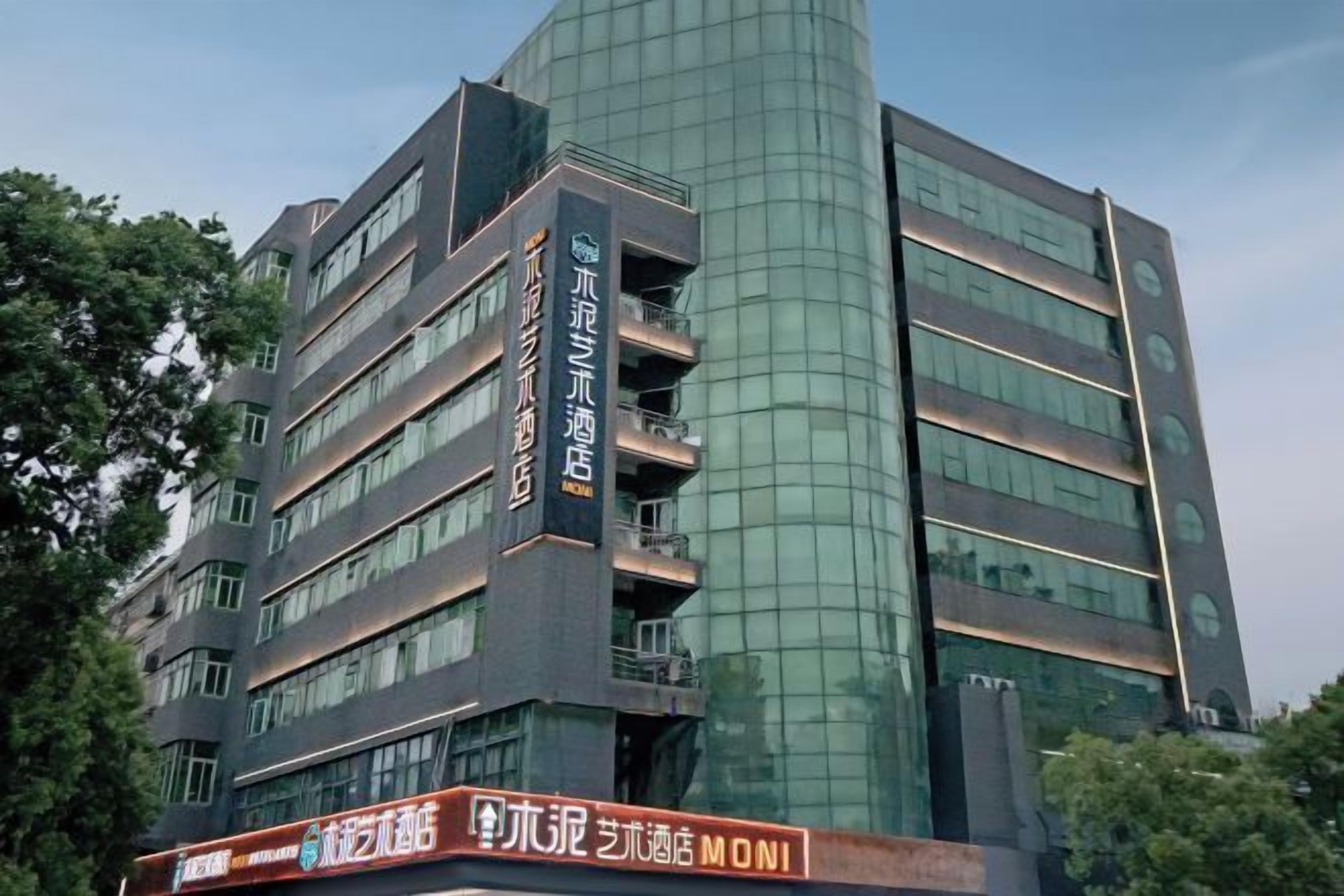 A multi-story hotel with a modern design, featuring a prominent vertical sign with text, multiple balconies, and a reflective glass facade.