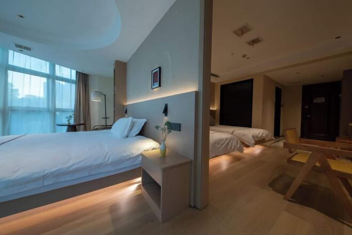 A modern hotel room with two beds, a bedside table with a vase, a desk with a chair, and a large window.
