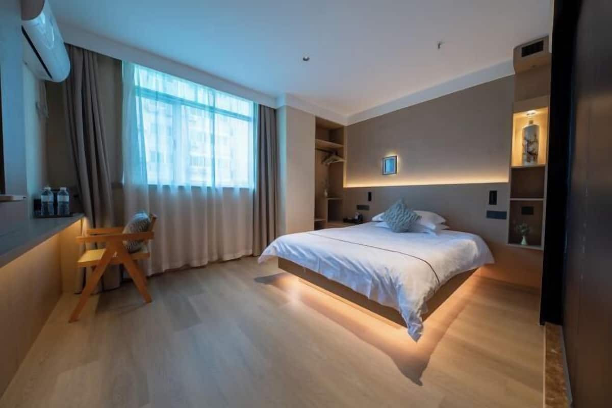 A modern hotel room with a large bed, a desk, and a wardrobe.