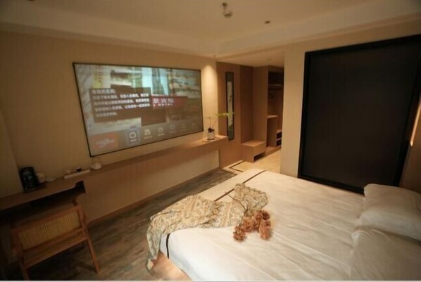 Habitación de hotel moderna con una cama grande, un televisor de pantalla plana montado en la pared, una silla de madera y una pequeña mesa con una planta.