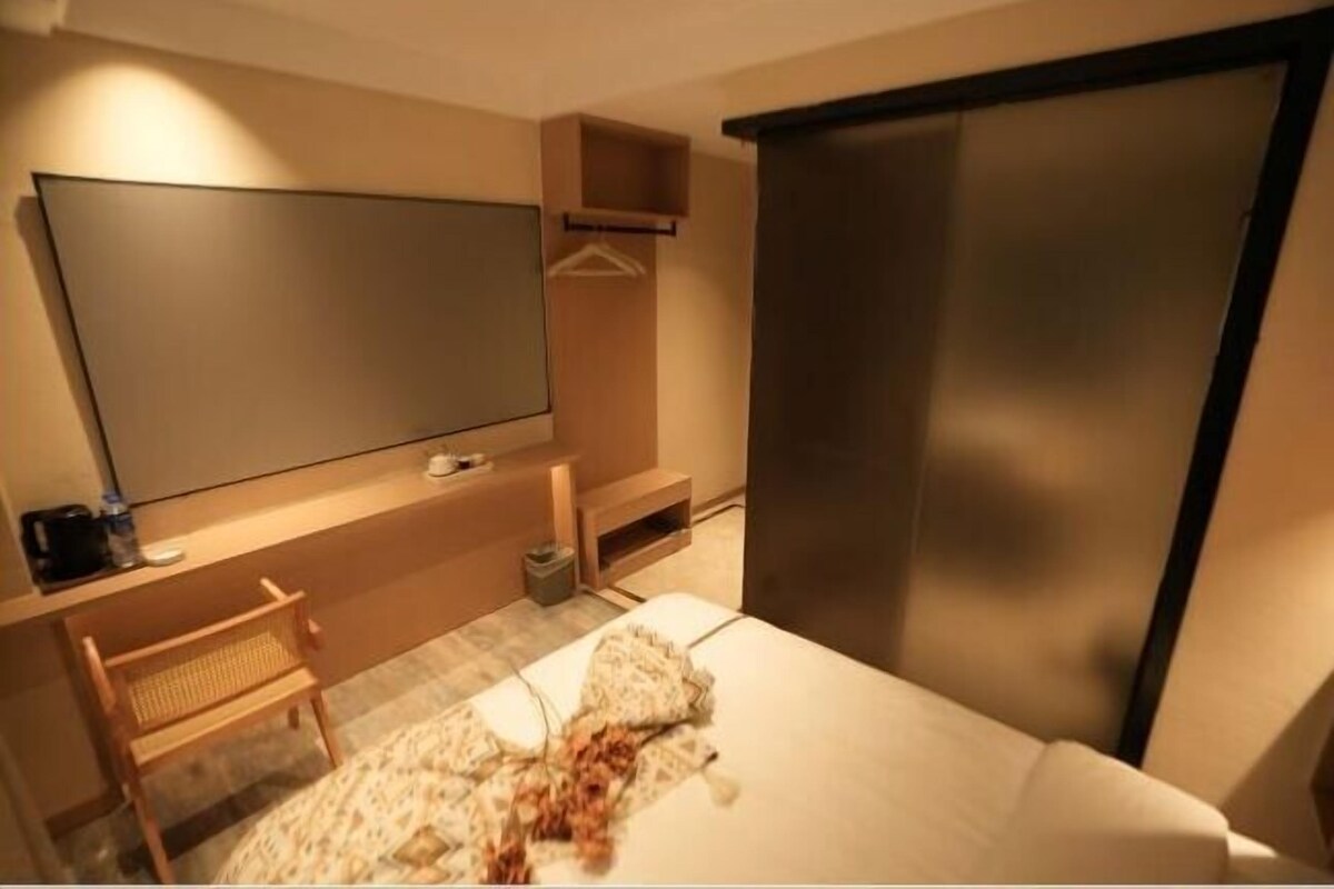 Una habitación de hotel con una cama, un escritorio con silla, un televisor y un armario.