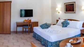 A hotel room with a bed, a desk, a chair, a television, and a dining table with breakfast items.