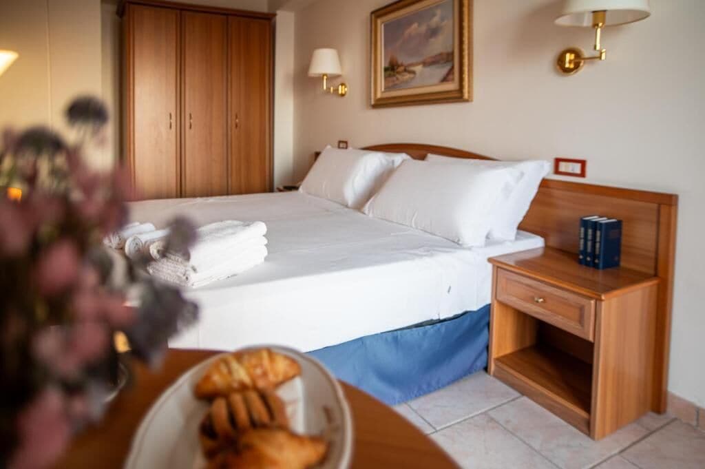 Ein Hotelzimmer mit einem Bett, einem Nachttisch mit Lampe, einem Holzschrank und einem Bild an der Wand.