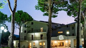 Un hotel de varios pisos con un cartel llamativo de 'BB', asientos al aire libre y árboles en primer plano.