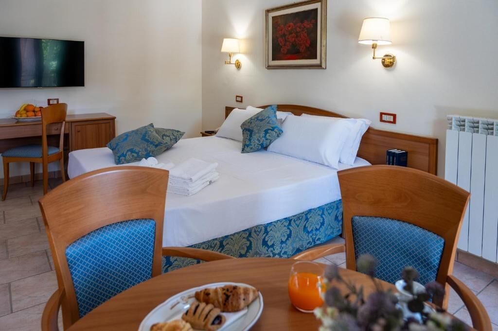 Ein Hotelzimmer mit Bett, Nachttischen, einem Schreibtisch mit Stuhl, einem Fernseher und einem Esstisch mit Stühlen.