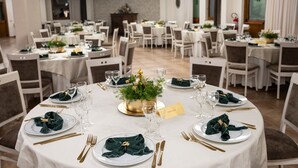 Un salón de banquetes con mesas redondas dispuestas para un evento formal, con manteles blancos, cubiertos dorados y servilletas verdes.