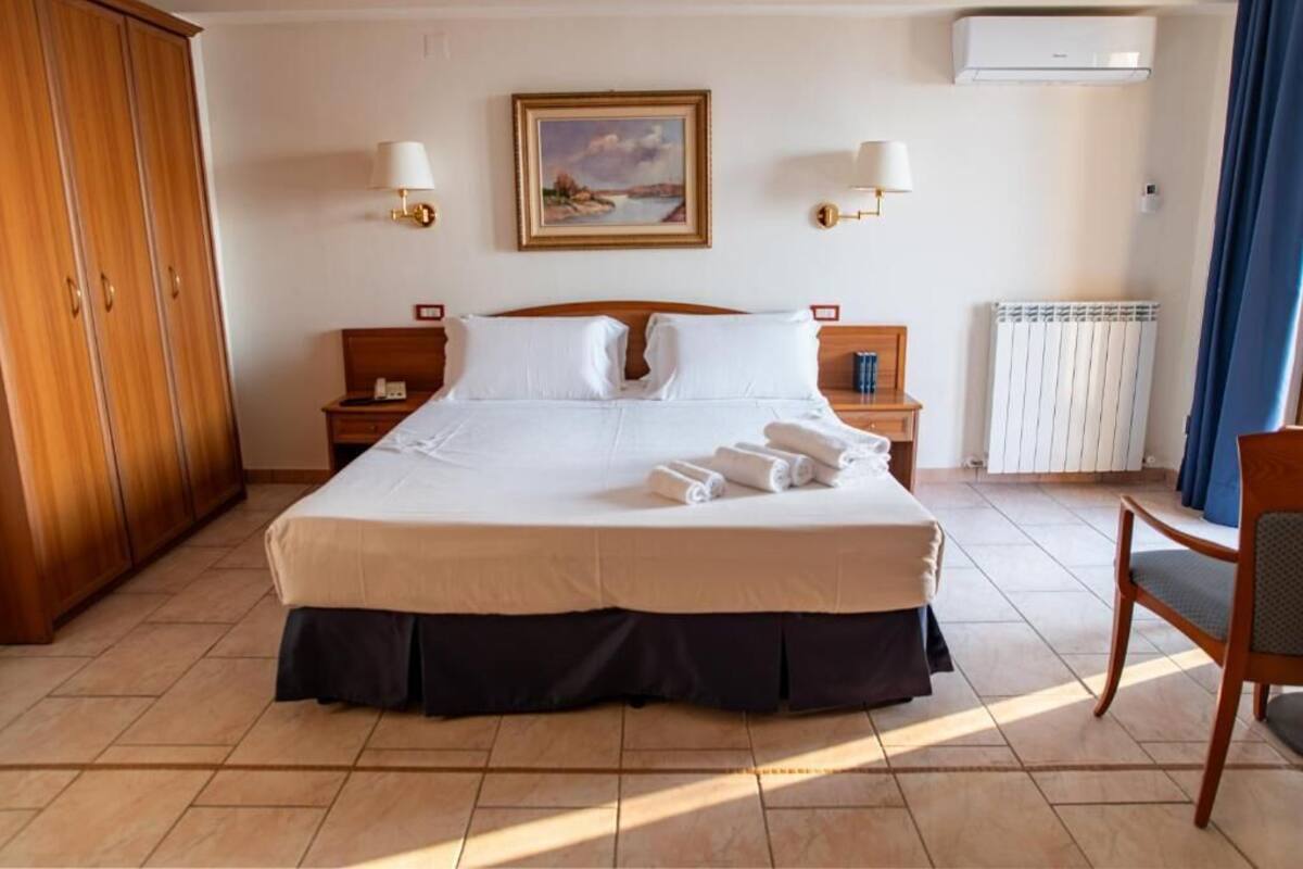 Habitación de hotel con una cama grande, dos mesitas de noche, un armario y un cuadro en la pared.