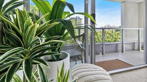 A balcony with a potted plant, wicker furniture, and a view of buildings. - Coastal Lights I Pool, Gym & Parking@HarbourLights (Cairns City)