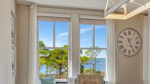 A room with a large window, a wooden table, wicker chairs, and a wall clock.