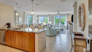 A spacious kitchen with a large island, modern lighting, and large windows offering a view of greenery.