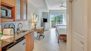 A compact hotel room with a kitchenette, a bed, a desk, and a view of the outdoors.