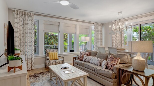 A spacious living room with a sofa, coffee table, and a TV. There are large windows with curtains, a ceiling fan, and a chandelier. - Bayview Luxury: Sandestin Retreat, Resort Perks (Miramar Beach)