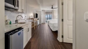 Eine moderne Küche mit weißen Schränken, einer eingebauten Mikrowelle und einem Kühlschrank. Ein Essbereich mit Tisch und Stühlen ist zu sehen. Der Raum hat einen Holzboden und einen Deckenventilator.
