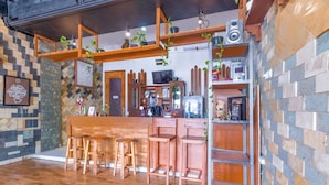 A bar area with wooden stools, a bar counter, and shelves with various items. - Hotel O Homestay Amanda Syariah (Makassar)