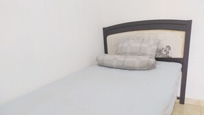 A single bed with a checkered pillow and a plain mattress in a room with a tiled floor and a plain wall. - Hotel O Homestay Amanda Syariah (Makassar)