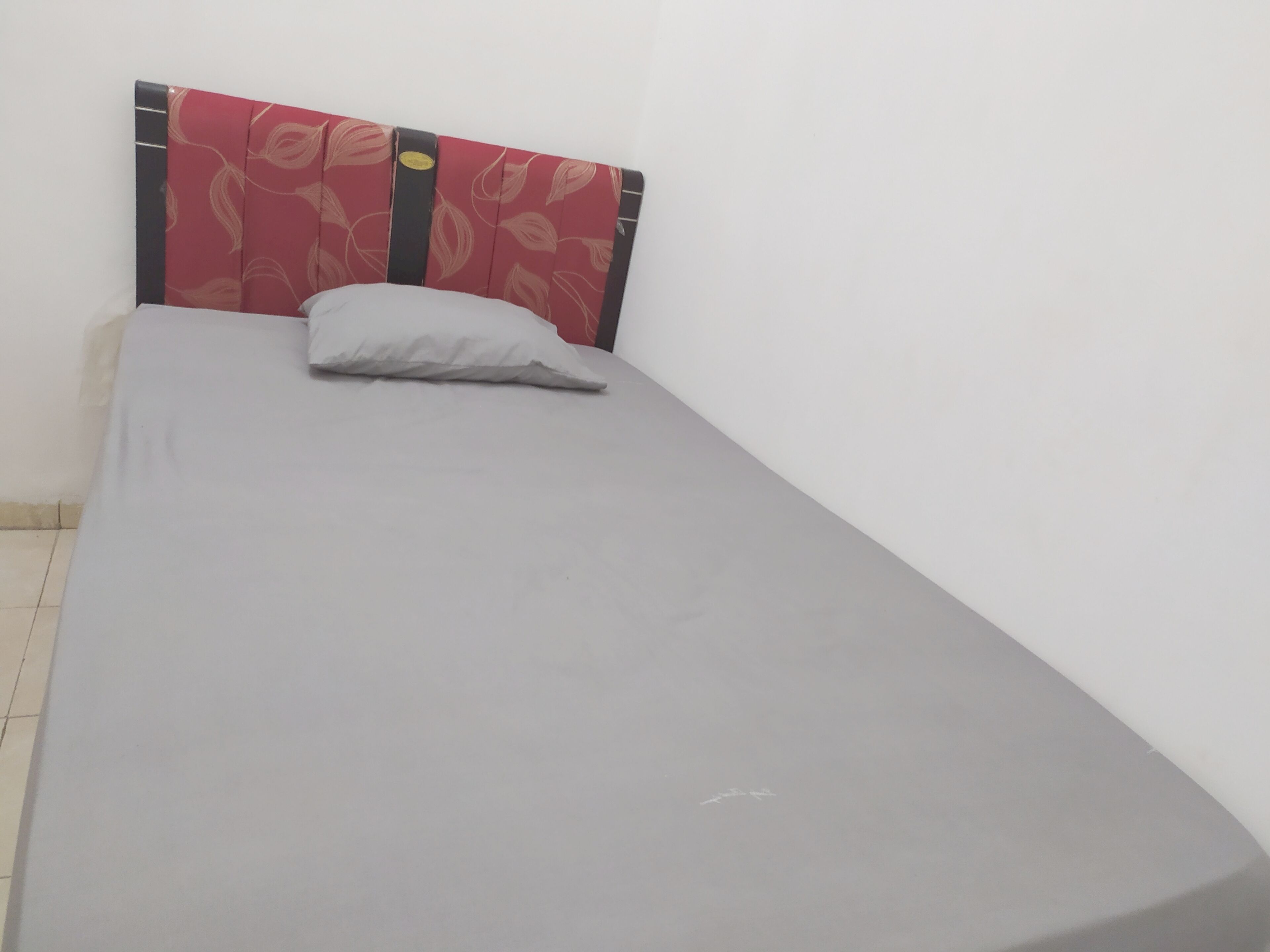 A single bed with a grey mattress and a red headboard with a leaf pattern.