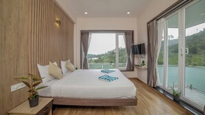A modern bedroom with a large bed, wooden paneling, a TV, and a balcony with a scenic view.