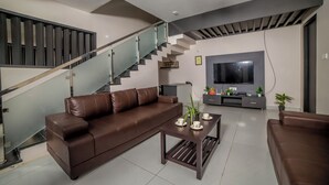 A modern living room with a brown leather sofa, a coffee table, and a flat-screen TV mounted on the wall.