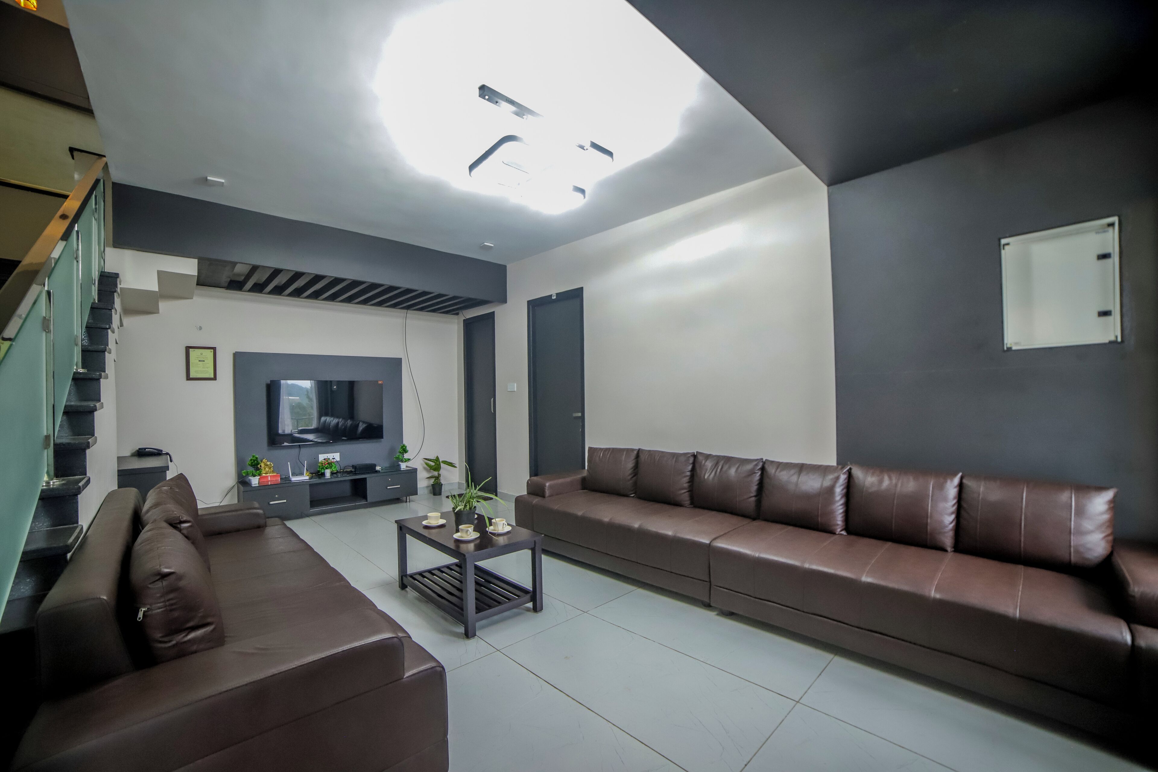 A modern living room with a brown leather sofa, a coffee table with decorative items, a flat-screen TV, and a staircase leading to an upper level.