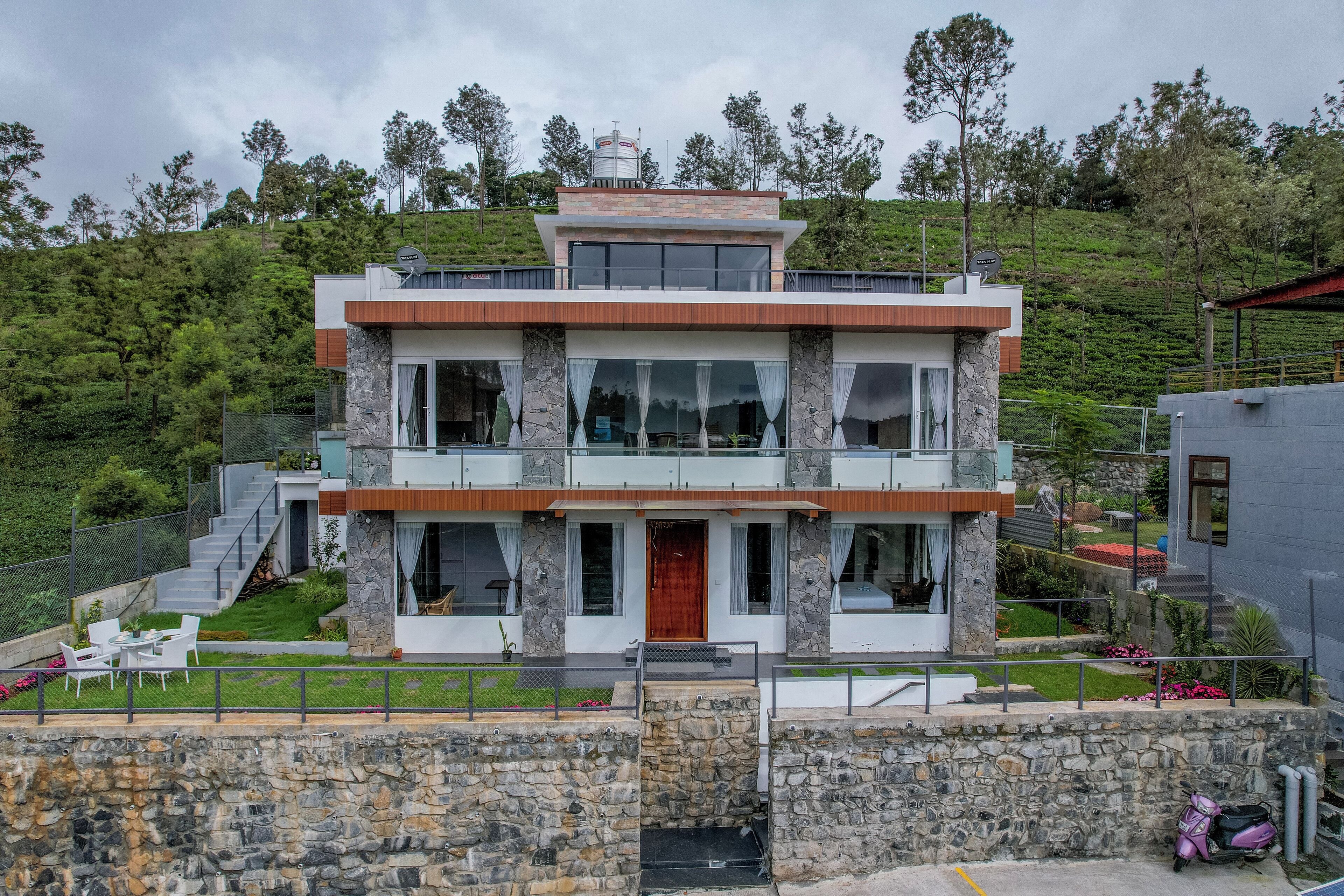 A two-story modern house with a stone facade, large windows, and a wooden front door.