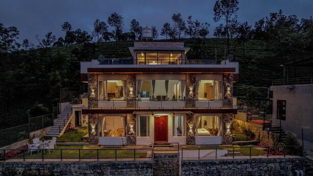 A modern two-story house with a stone facade, multiple balconies, and a well-lit entrance.