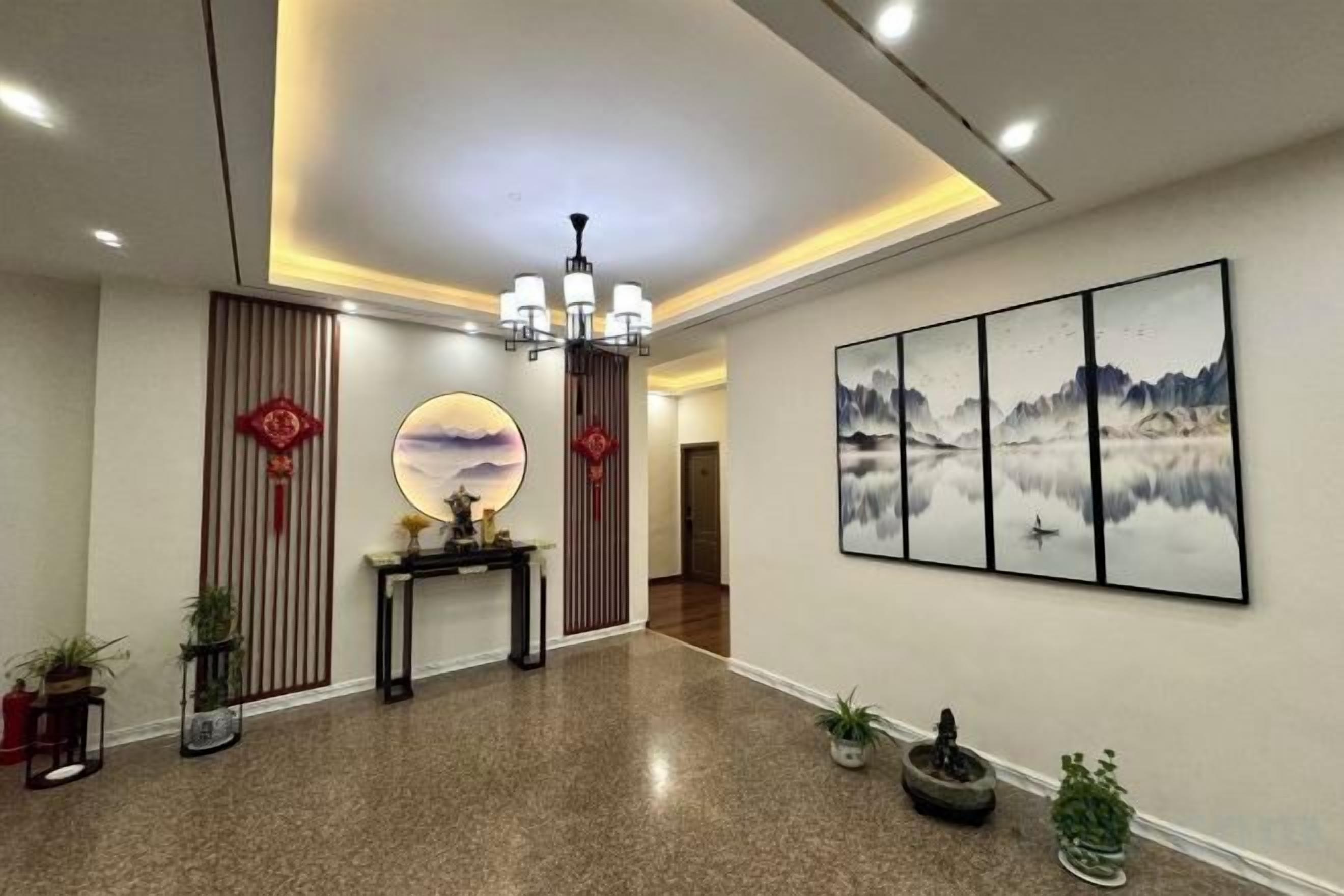 A hotel lobby with a reception desk, a chandelier, wall art, and potted plants.