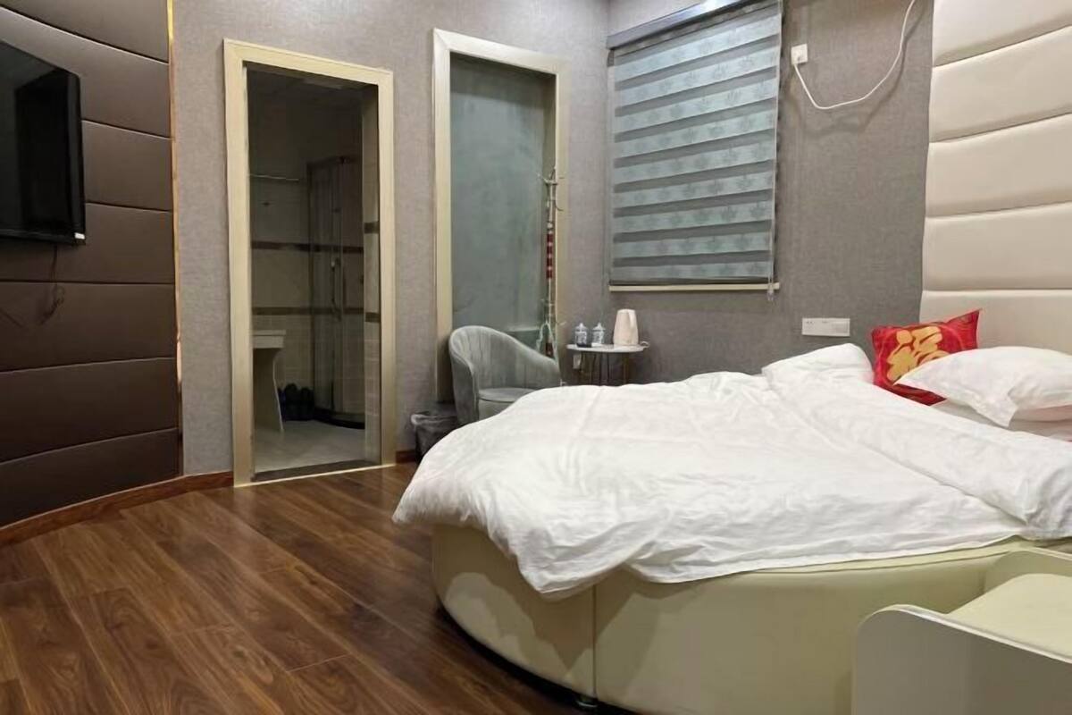 A modern bedroom with a curved bed, a walk-in closet, and a bathroom with a shower and toilet.