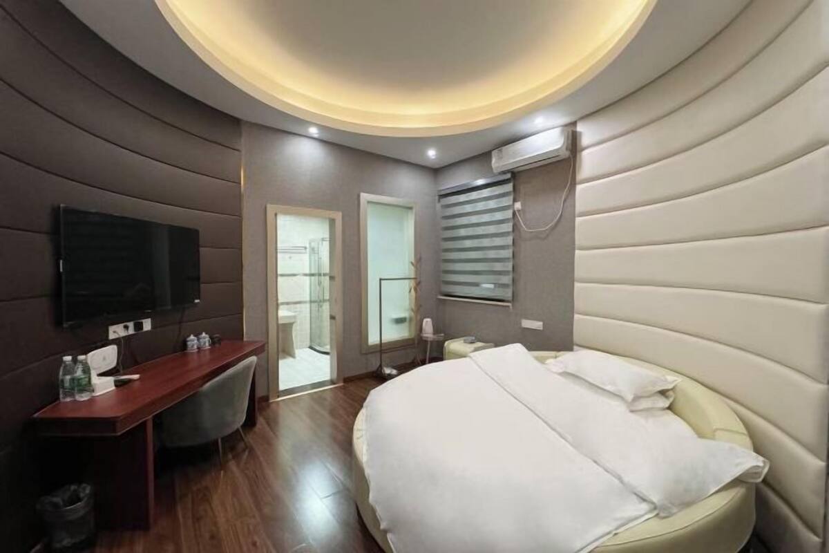 A modern hotel room with a curved ceiling, a bed, a desk, and a television.