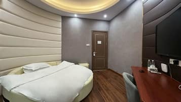 A hotel room with a bed, a desk, a television, and a door.