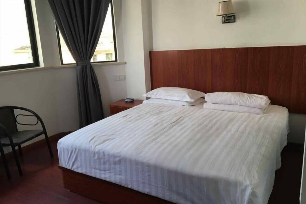 A hotel room with a bed, a chair, a nightstand, a lamp, and a window with curtains.
