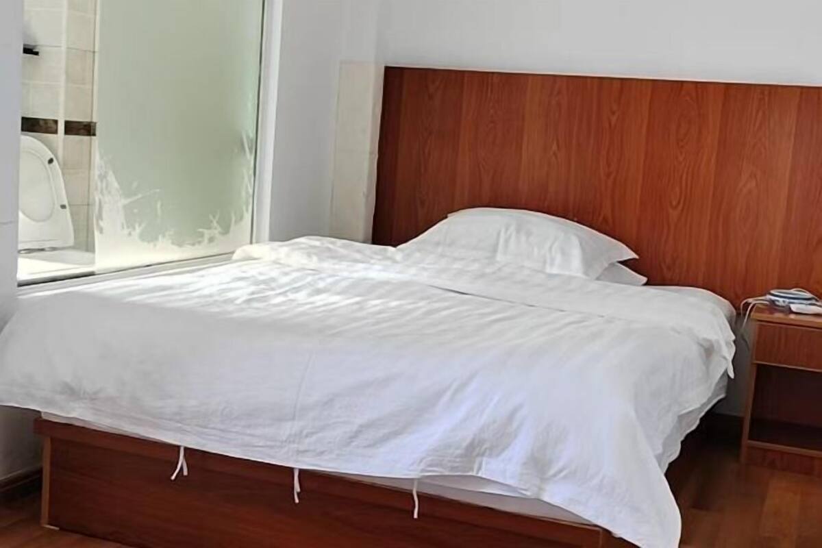 A neatly made bed with white bedding, a wooden headboard, and a bedside table with a book.