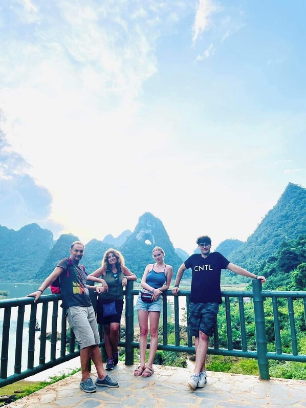 A group of people standing on a stone platform with a railing, overlooking a mountainous landscape with a body of water in the background. - Cao Bang Loop Hostel (Tan Giang)