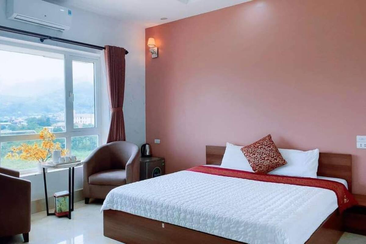 Una habitación de hotel con una cama grande, una silla, una mesita y una ventana con cortinas.