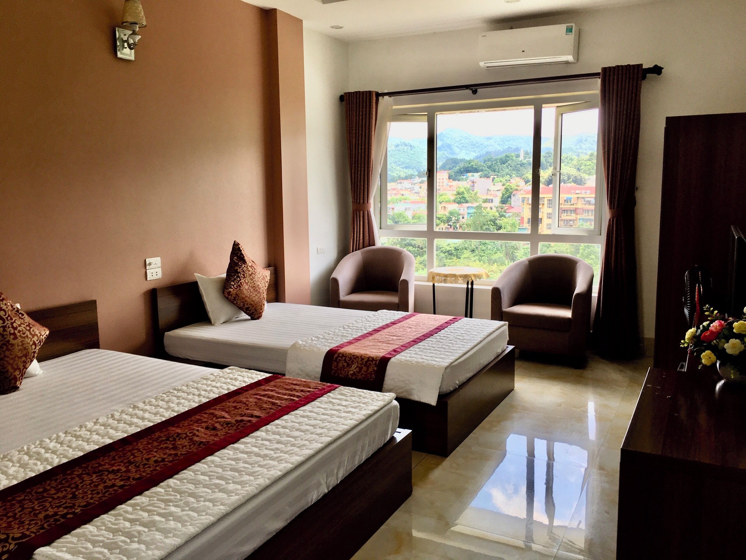 A hotel room with two beds, a small table, and two armchairs.