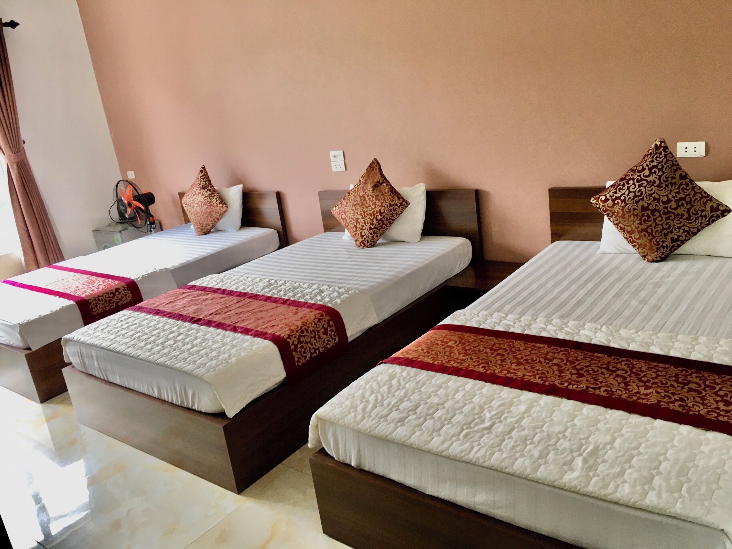 A hotel room with three single beds, each with a patterned pillow and a red and white bedspread.