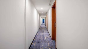 Un pasillo con alfombra estampada, paredes blancas y puertas de madera.