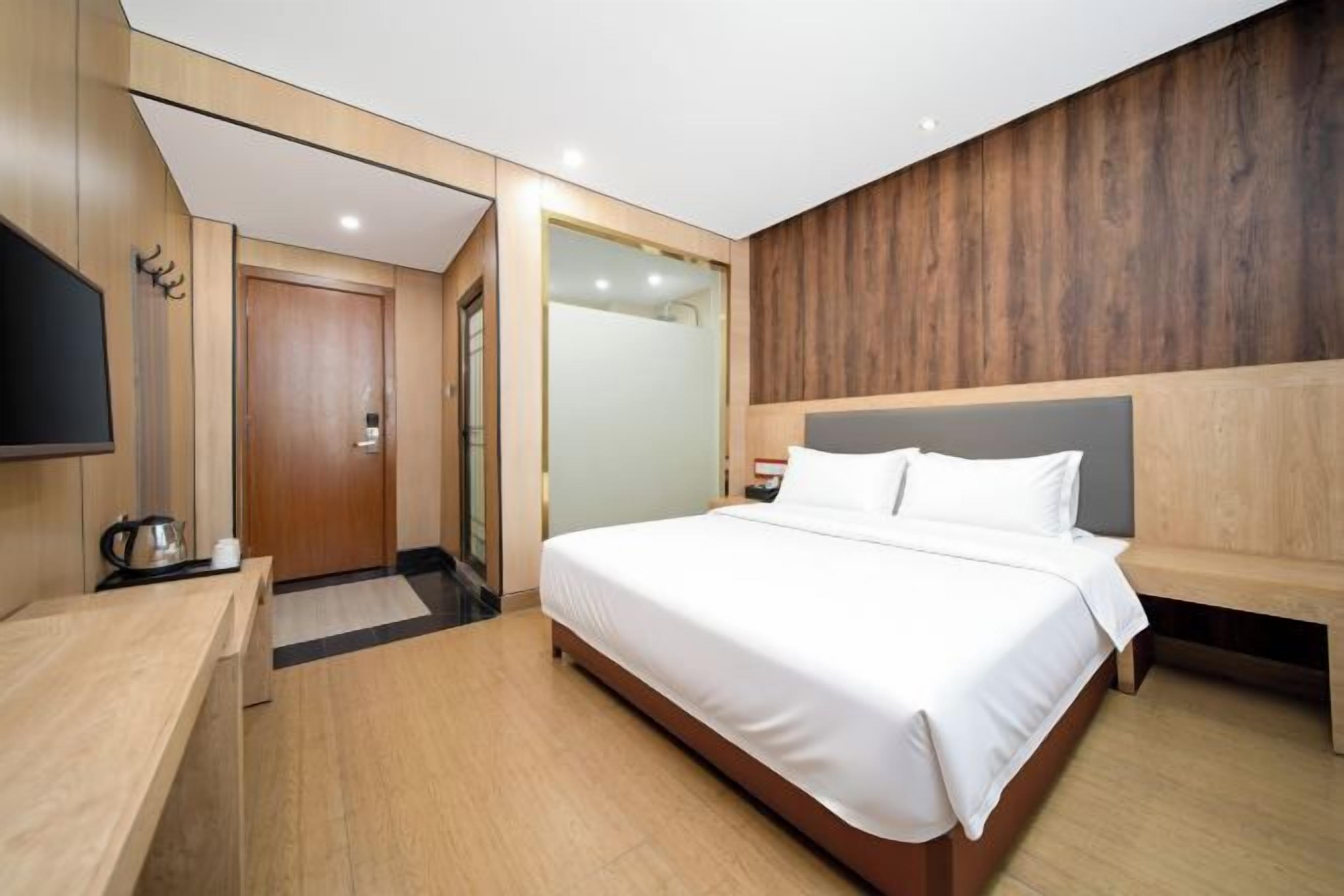 Ein modernes Hotelzimmer mit einem Holzkopfteil, einem Flachbildfernseher, einem Holztisch und einem großen Bett.