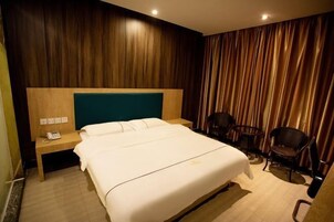 Habitación de hotel con una cama grande, cabecera de madera, mesita de noche con un teléfono, dos sillas y un fondo de cortina.