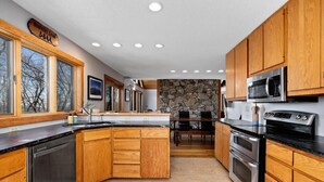 A modern kitchen with wooden cabinets, a central island, a stone accent wall, and a dining area with a table and chairs. - Nowhere Land with Wintergreen Advantage (Wintergreen)