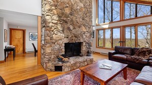 A spacious living room with a stone fireplace, leather furniture, and large windows offering a view of the outdoors. - Nowhere Land with Wintergreen Advantage (Wintergreen)