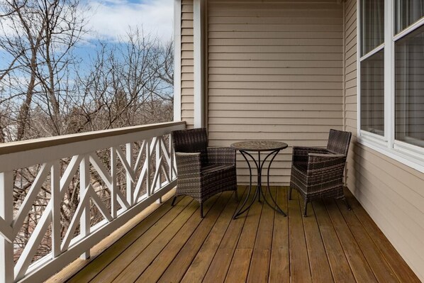 A wooden deck with a white railing, two wicker chairs, and a small round table.