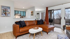Ein modernes Wohnzimmer mit einem braunen Ledersofa, einem weißen Couchtisch und einer Küche im Hintergrund.