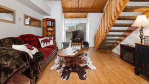 Un salon chaleureux avec un canapé rouge, un plafond en bois, un escalier et un tapis en peau de vache.